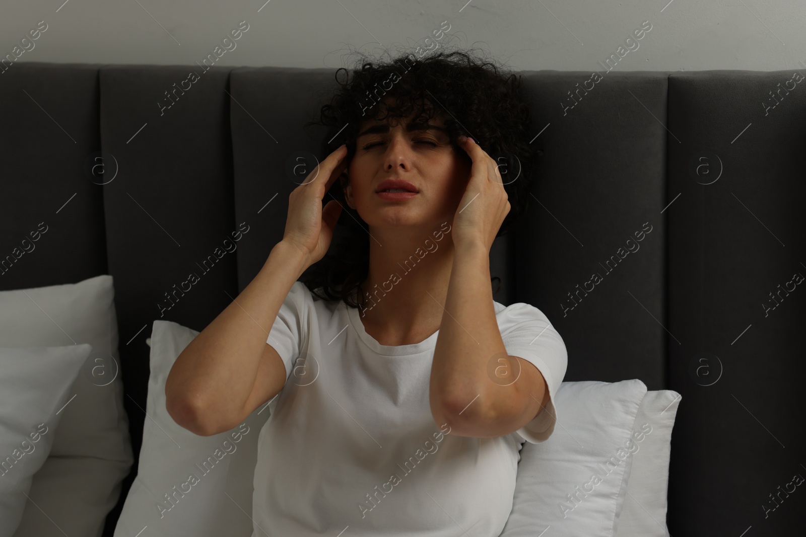 Photo of Young woman suffering from headache in bed at night