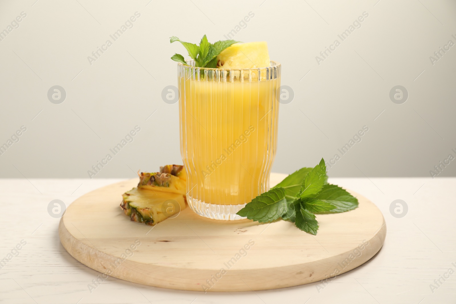 Photo of Glass of tasty pineapple cocktail, mint and sliced fruit on white table