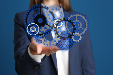 Image of Businesswoman demonstrating gear mechanism on blue background, closeup