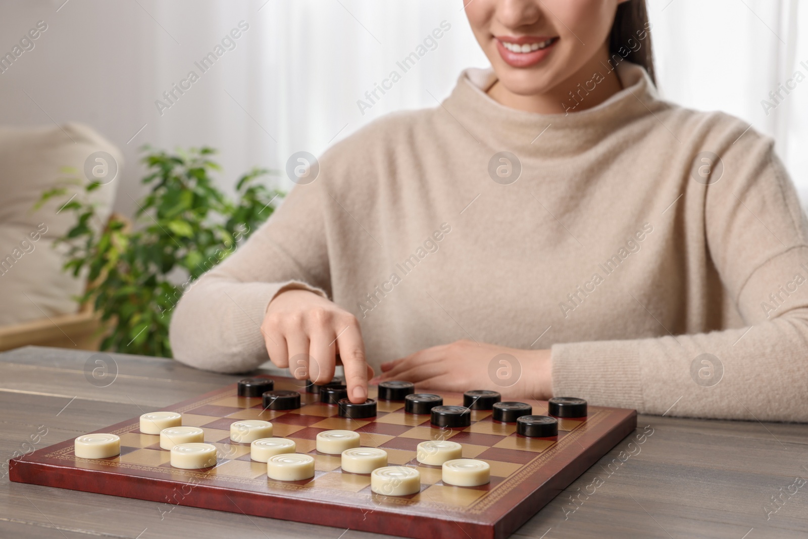 Photo of Playing checkers. Woman thinking about next move at table in room, closeup