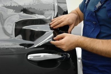 Photo of Worker tinting car window with foil in workshop, closeup