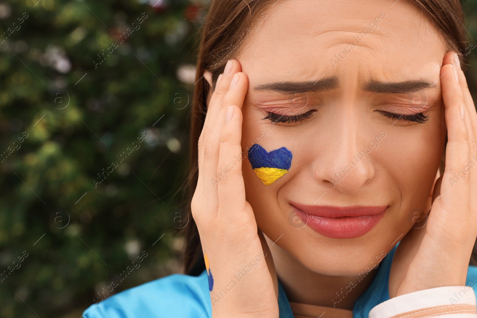 Photo of Sad young woman with drawing of Ukrainian flag on face outdoors, closeup. Space for text