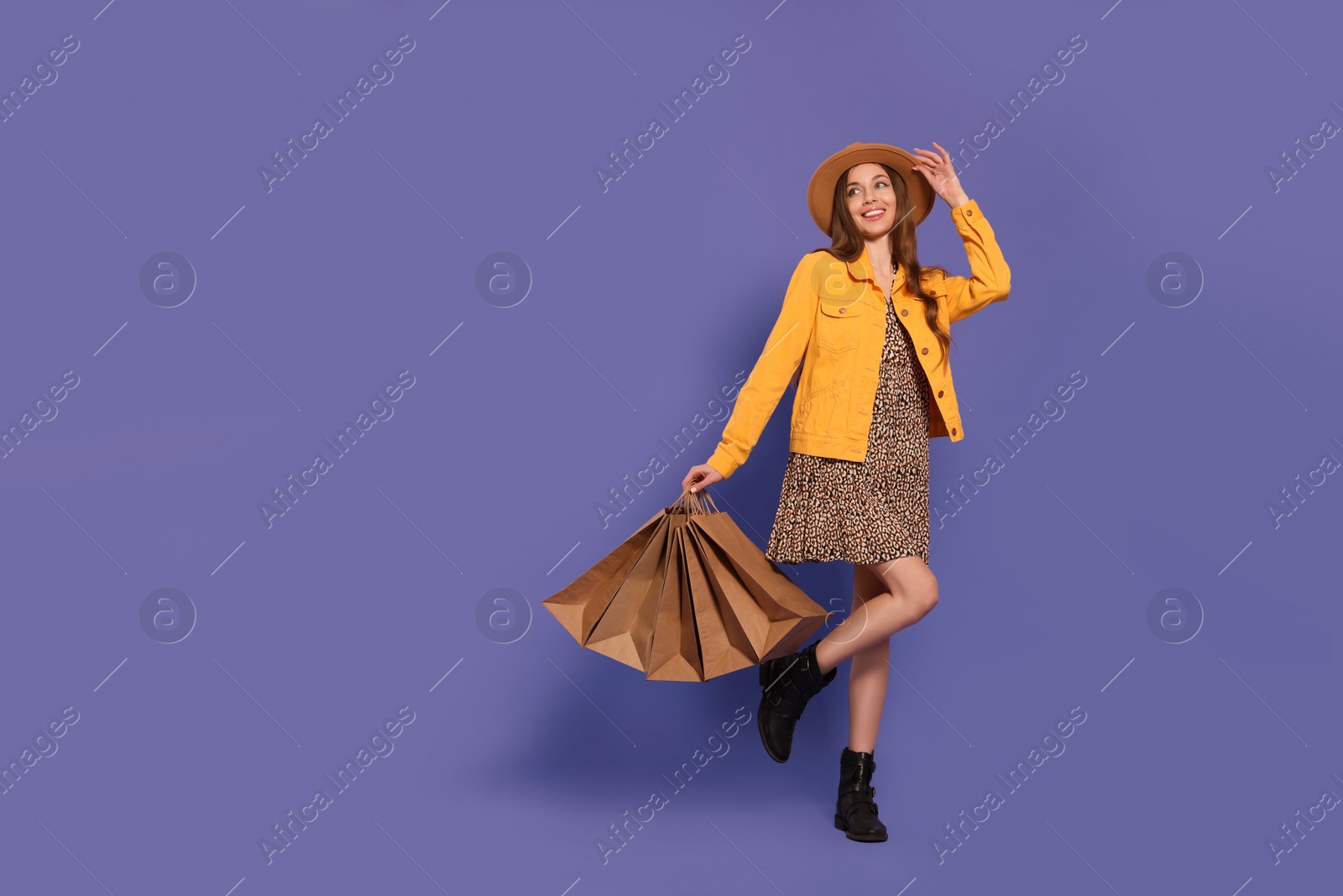 Photo of Stylish young woman with shopping bags on purple background, space for text