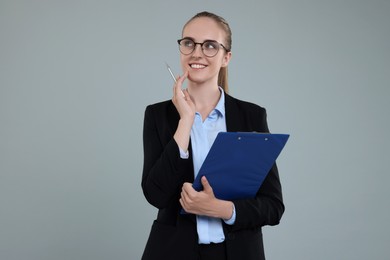 Photo of Happy young secretary with clipboard and pen on grey background