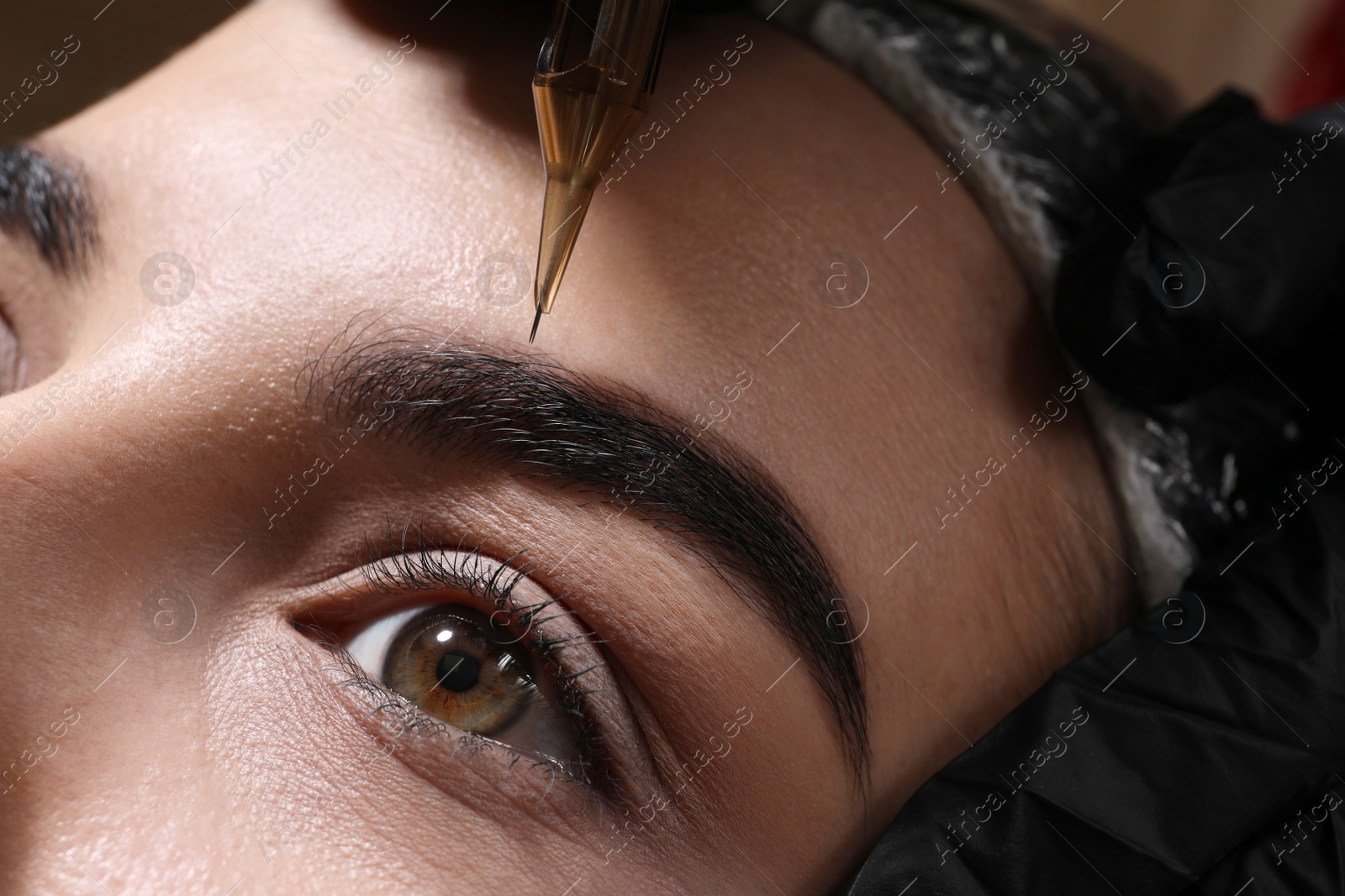 Photo of Young woman undergoing procedure of permanent eyebrow makeup in tattoo salon, closeup