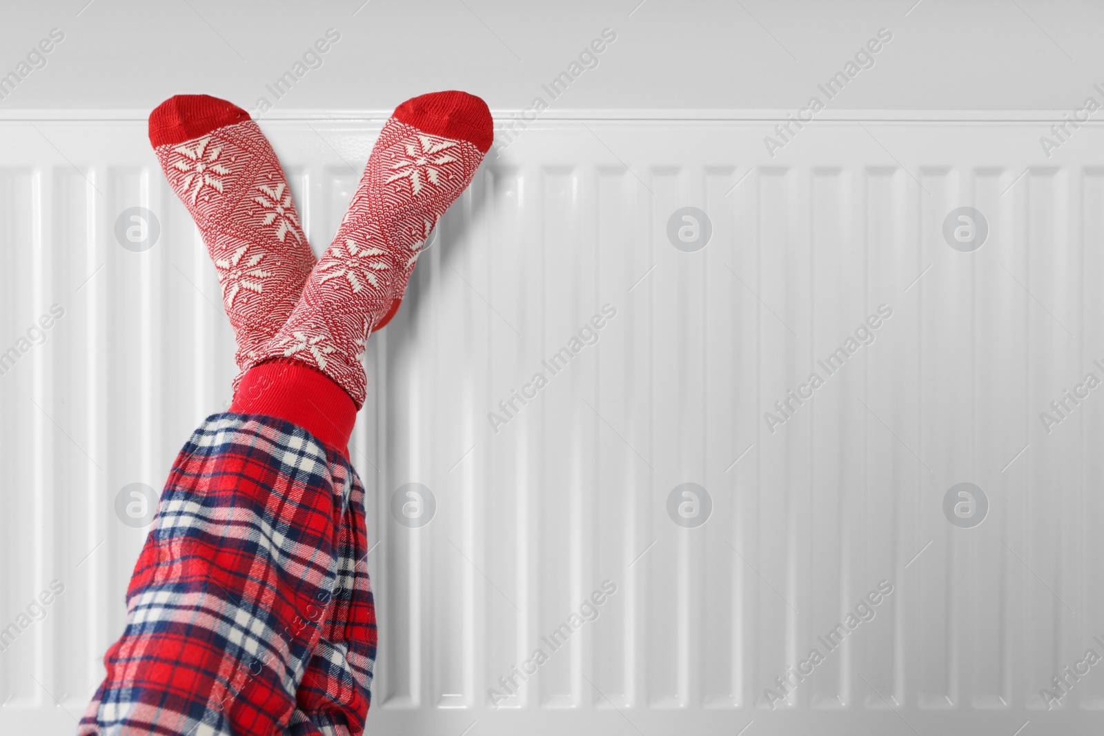 Photo of Little girl warming feet near heating radiator indoors, closeup. Space for text