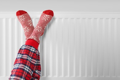 Little girl warming feet near heating radiator indoors, closeup. Space for text