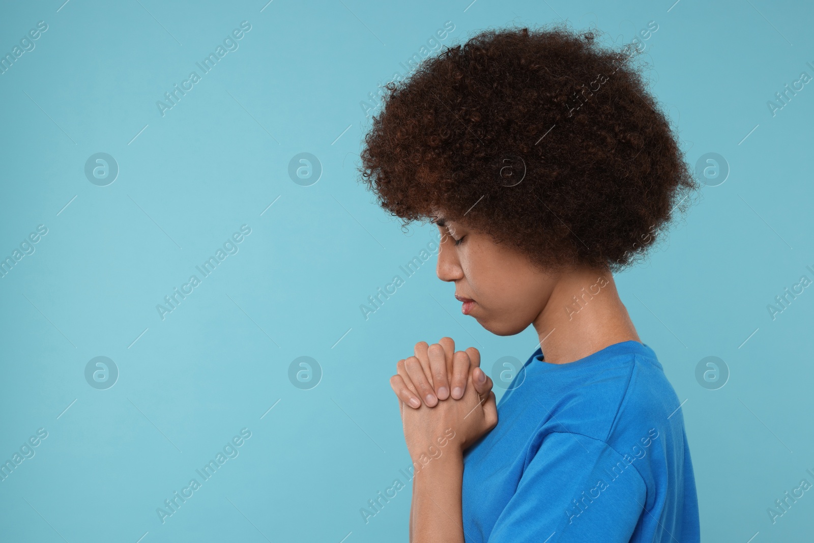 Photo of Woman with clasped hands praying to God on light blue background. Space for text