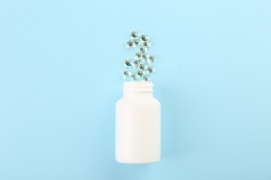 Bottle and vitamin capsules on light blue background, top view