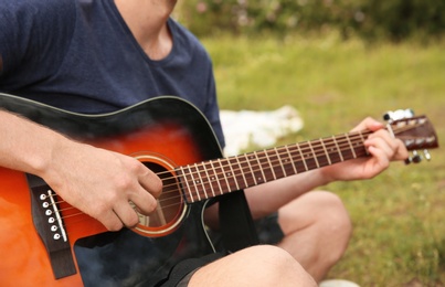 Photo of Young man playing guitar in wilderness. Camping season