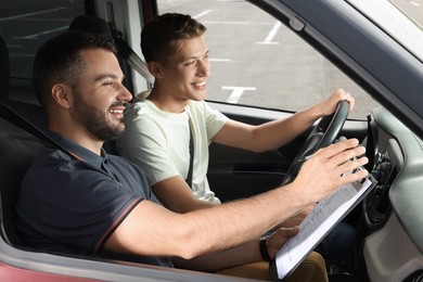 Photo of Driving school. Happy student passing driving test with examiner in car at parking lot