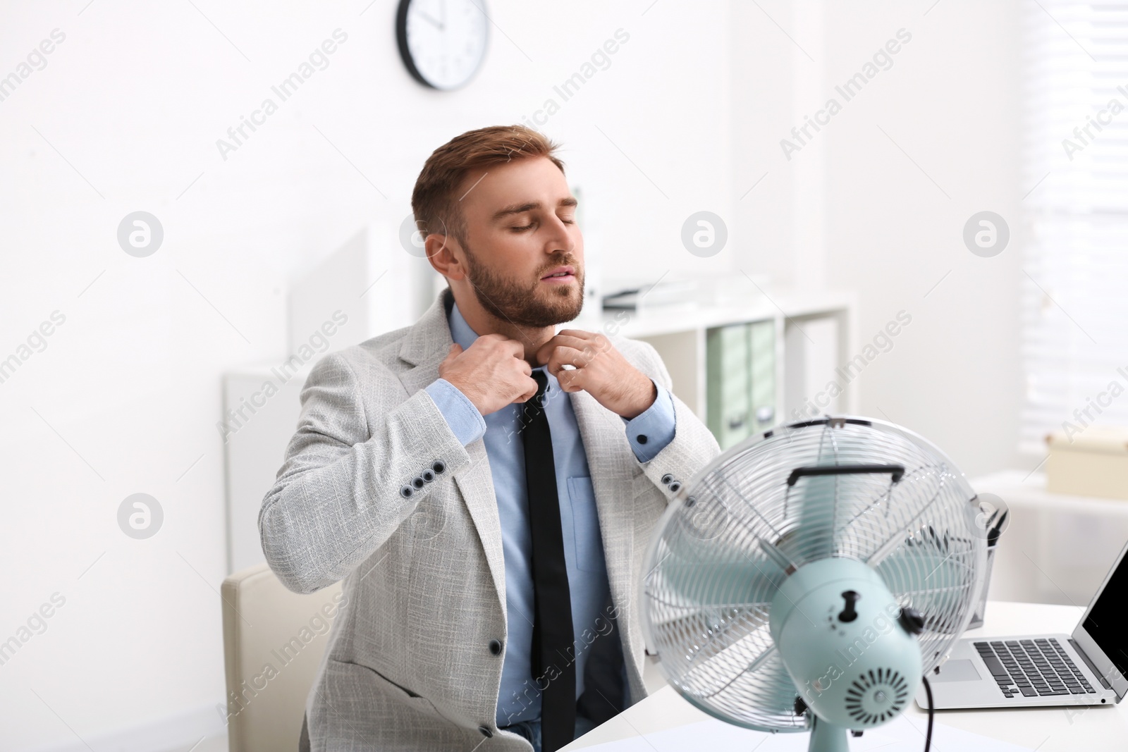 Photo of Man enjoying air flow from fan at workplace