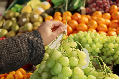 Photo of Woman holding fresh grapes near fruit counter at market, closeup