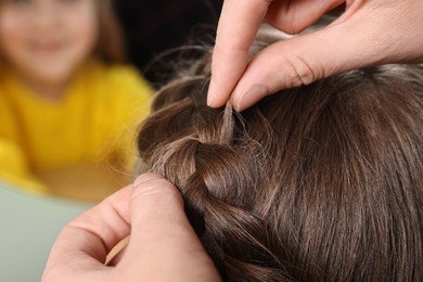 Professional stylist braiding girl's hair indoors, closeup