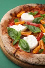 Delicious pizza with burrata cheese, tomatoes and basil on green background, closeup