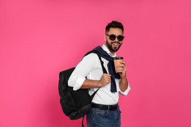 Photo of Young man with stylish backpack and cup of coffee on pink background