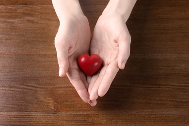 Photo of Woman holding small red heart on wooden table. Heart attack concept