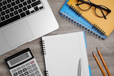 Photo of Notebook, calculator, laptop, glasses and stationery on wooden table, flat lay