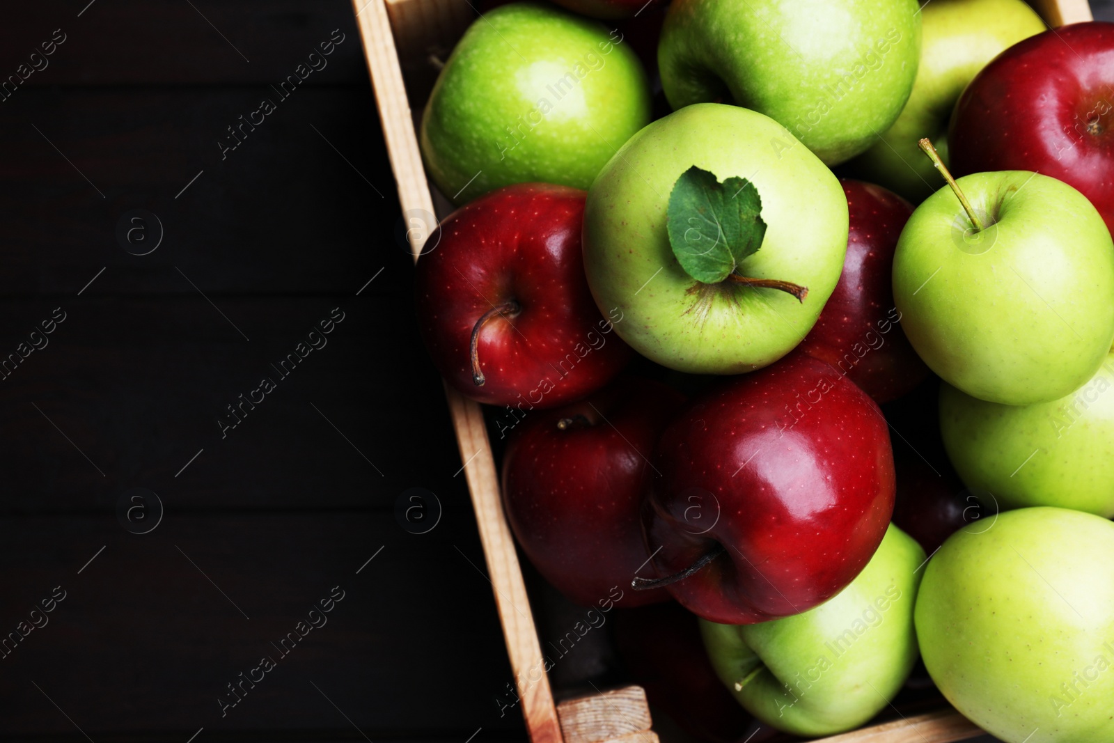 Photo of Fresh ripe red and green apples in wooden crate on black table, top view. Space for text