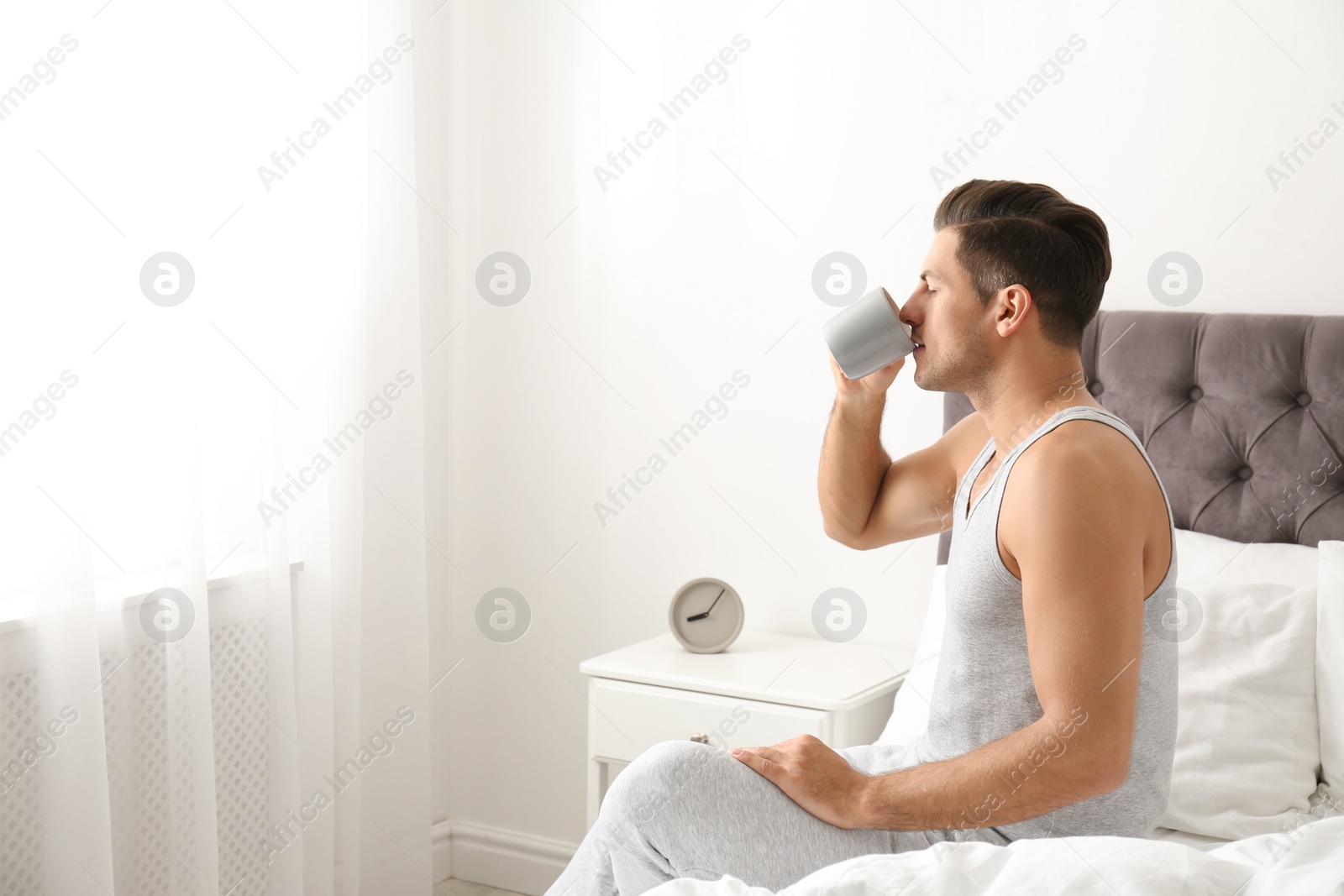 Photo of Man with cup of coffee in bedroom. Lazy morning