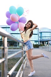 Photo of Beautiful young woman with color balloons on city street