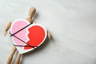 Wooden puppet with symbol of broken heart on gray background, space for text. Relationship problems