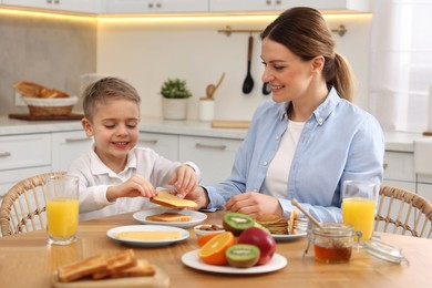 Mother and her cute little son having breakfast at table in kitchen