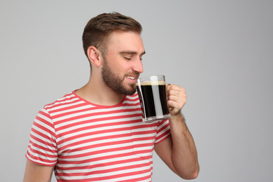 Photo of Handsome man with cold kvass on light grey background. Traditional Russian summer drink