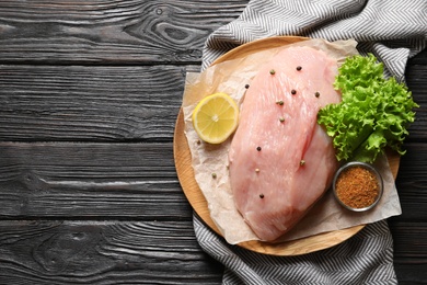 Photo of Plate with raw turkey fillet and ingredients on wooden background, top view. Space for text