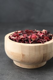 Photo of Hibiscus tea. Wooden bowl with dried roselle calyces on grey table, closeup