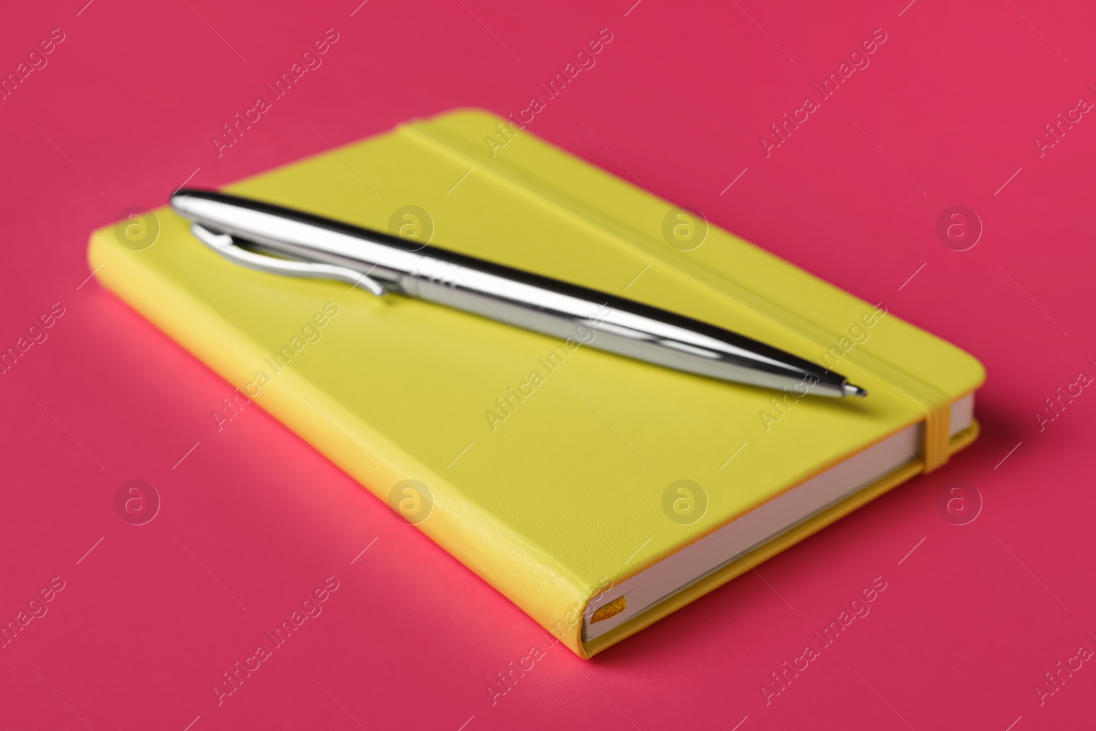 Photo of New stylish planner with hard cover and pen on pink background, closeup