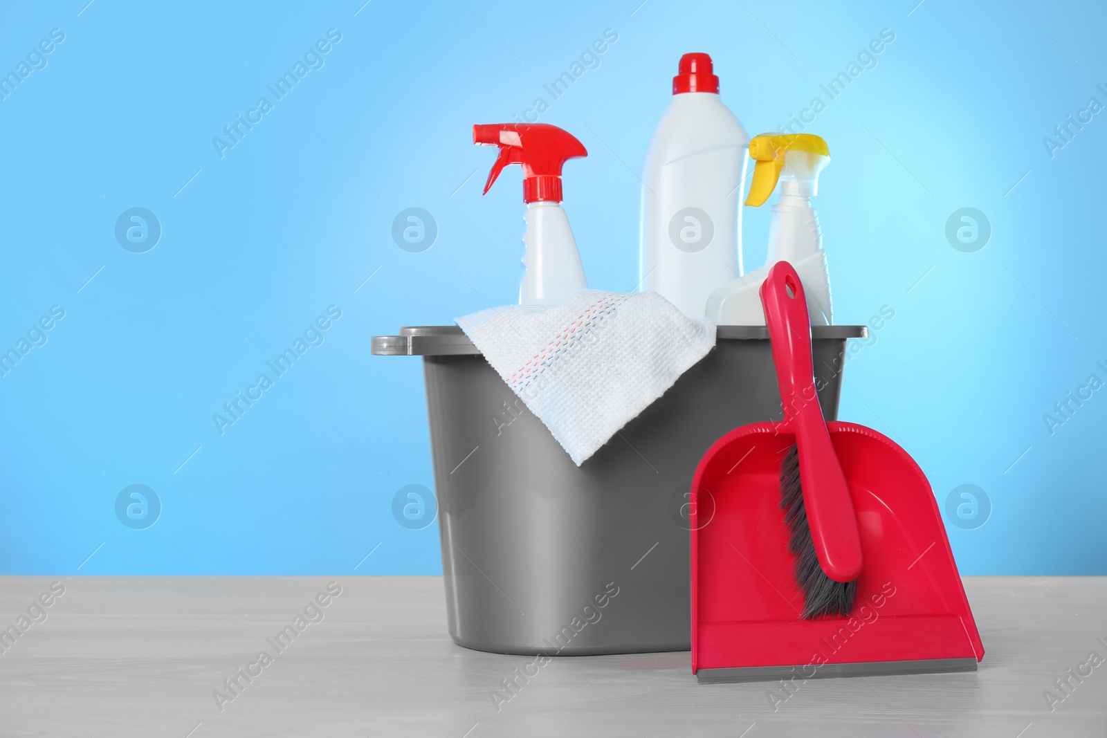 Photo of Bucket with different cleaning products and supplies on light table. Space for text