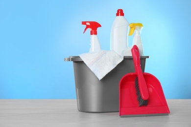 Photo of Bucket with different cleaning products and supplies on light table. Space for text