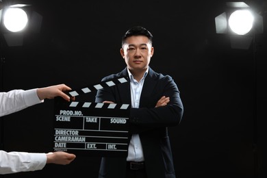 Photo of Asian actor performing while second assistant camera holding clapperboard on stage. Film industry