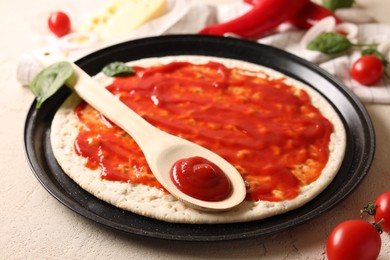 Pizza base smeared with sauce and tomatoes on light textured table, closeup