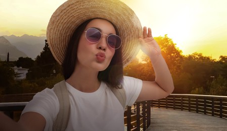 Image of Smiling young woman in sunglasses and straw hat taking selfie in park