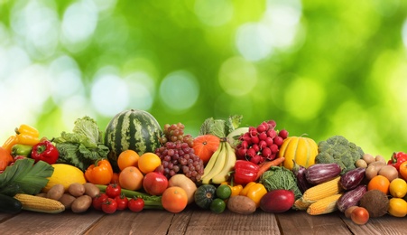 Image of Assortment of fresh organic vegetables and fruits on wooden table against blurred green background 