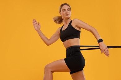 Woman exercising with elastic resistance band on orange background, low angle view