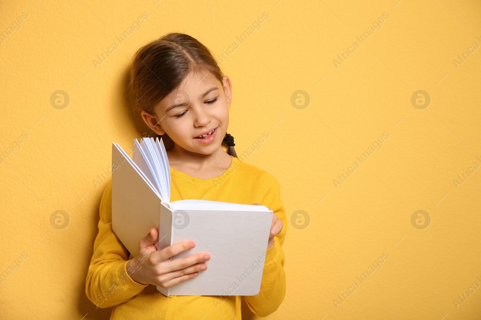 Photo of Cute little girl reading book on color background, space for text