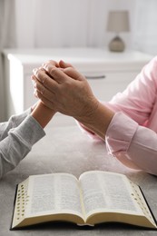 Photo of Boy and his godparent praying together at grey table indoors, closeup
