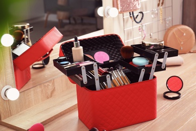 Beautician case with professional makeup products and tools on wooden dressing table