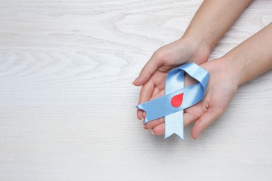 Woman holding light blue ribbon with paper blood drop at wooden table, top view and space for text. Diabetes awareness