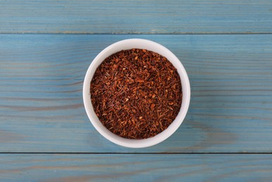 Photo of Dry rooibos leaves in bowl on turquoise wooden table, top view