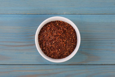 Dry rooibos leaves in bowl on turquoise wooden table, top view