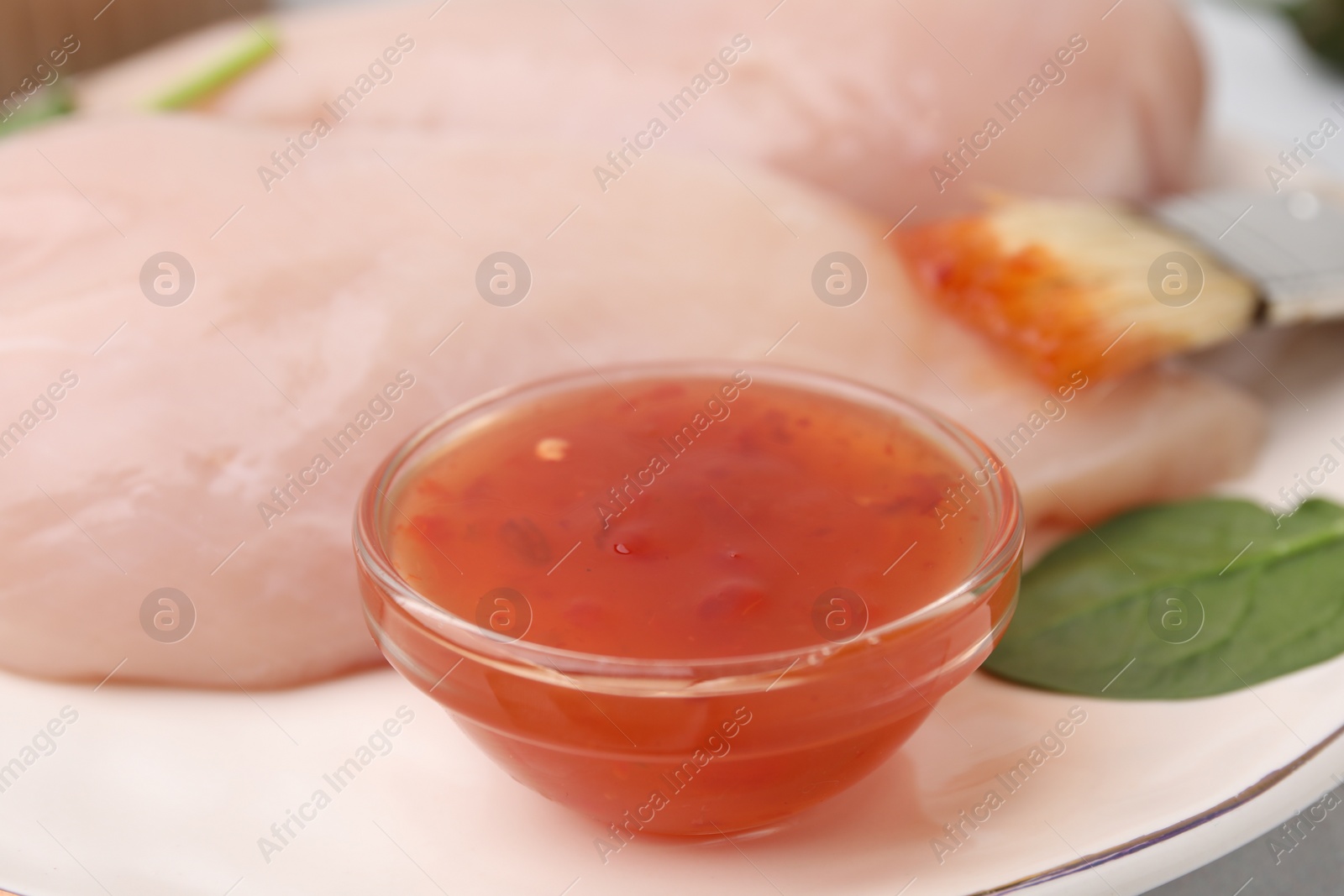 Photo of Marinade, basting brush and raw chicken fillets on table, closeup