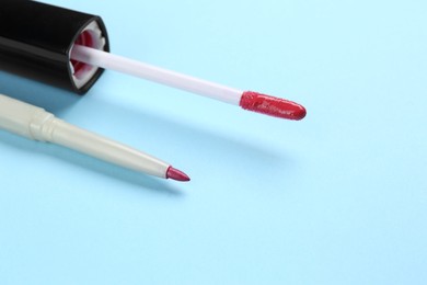 Photo of Lip pencil and brush of liquid lipstick on light blue background, closeup. Cosmetic product