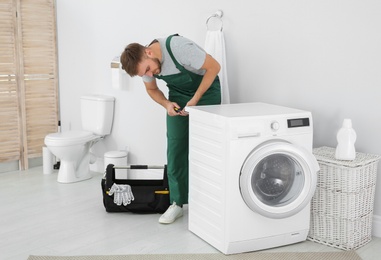 Photo of Young plumber fixing washing machine in bathroom