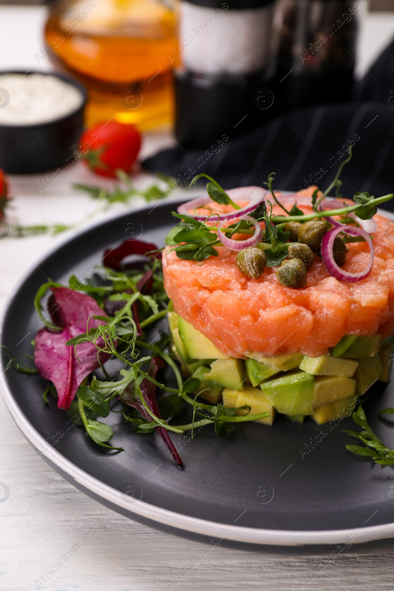 Photo of Tasty salmon tartare with avocado and greens on white wooden table, closeup. Space for text