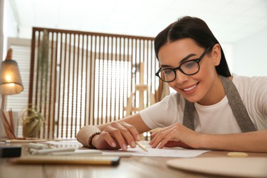 Photo of Young woman drawing with pencil at table indoors. Space for text