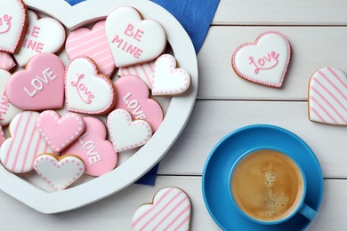 Delicious heart shaped cookies and cup of coffee on white wooden table, flat lay